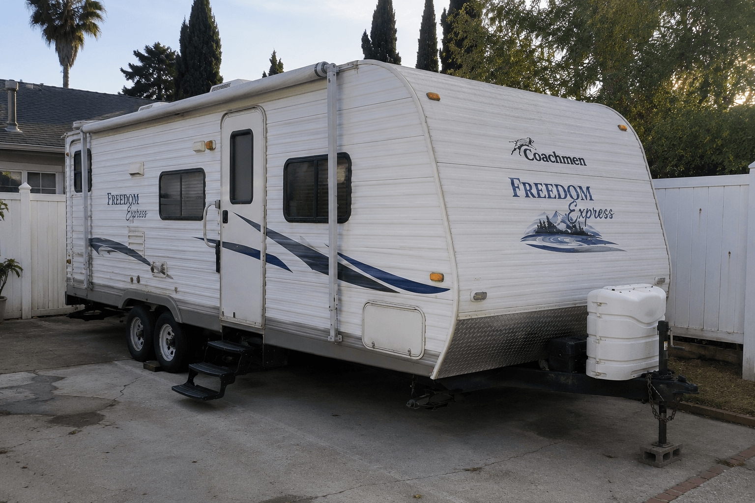 2009 Coachmen Freedom Express travel trailer parked in a California driveway with palm trees, white exterior with Coachmen logo and blue Freedom Express swoop graphic